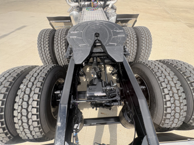 Back view of a Mack PI64T truck chassis showing drive axles and suspension components, fifth wheel, and dual rear axles with heavy-duty tires.