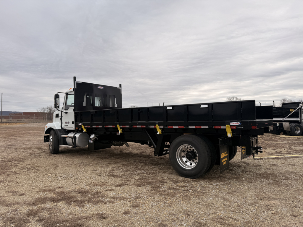 Flatbed truck, side view showing cargo bed and dual rear wheels with yellow tie-down straps and Mack MD7 cab in white.