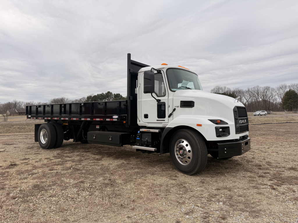 Mack MD7 flatbed truck showing cab and long black dump bed with side rails, white cab, front wheels, and overcast sky.