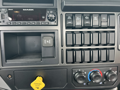 Mack MD7 cabin dashboard showing radio, empty tray, blank switches, and climate controls with yellow parking brake knob visible.