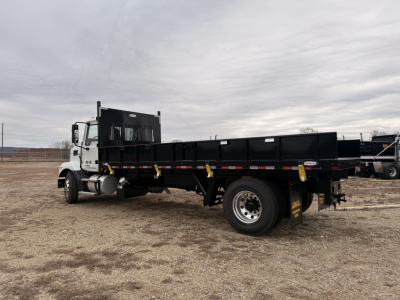 Flatbed truck, side view showing cargo bed and dual rear wheels with yellow tie-down straps and Mack MD7 cab in white.