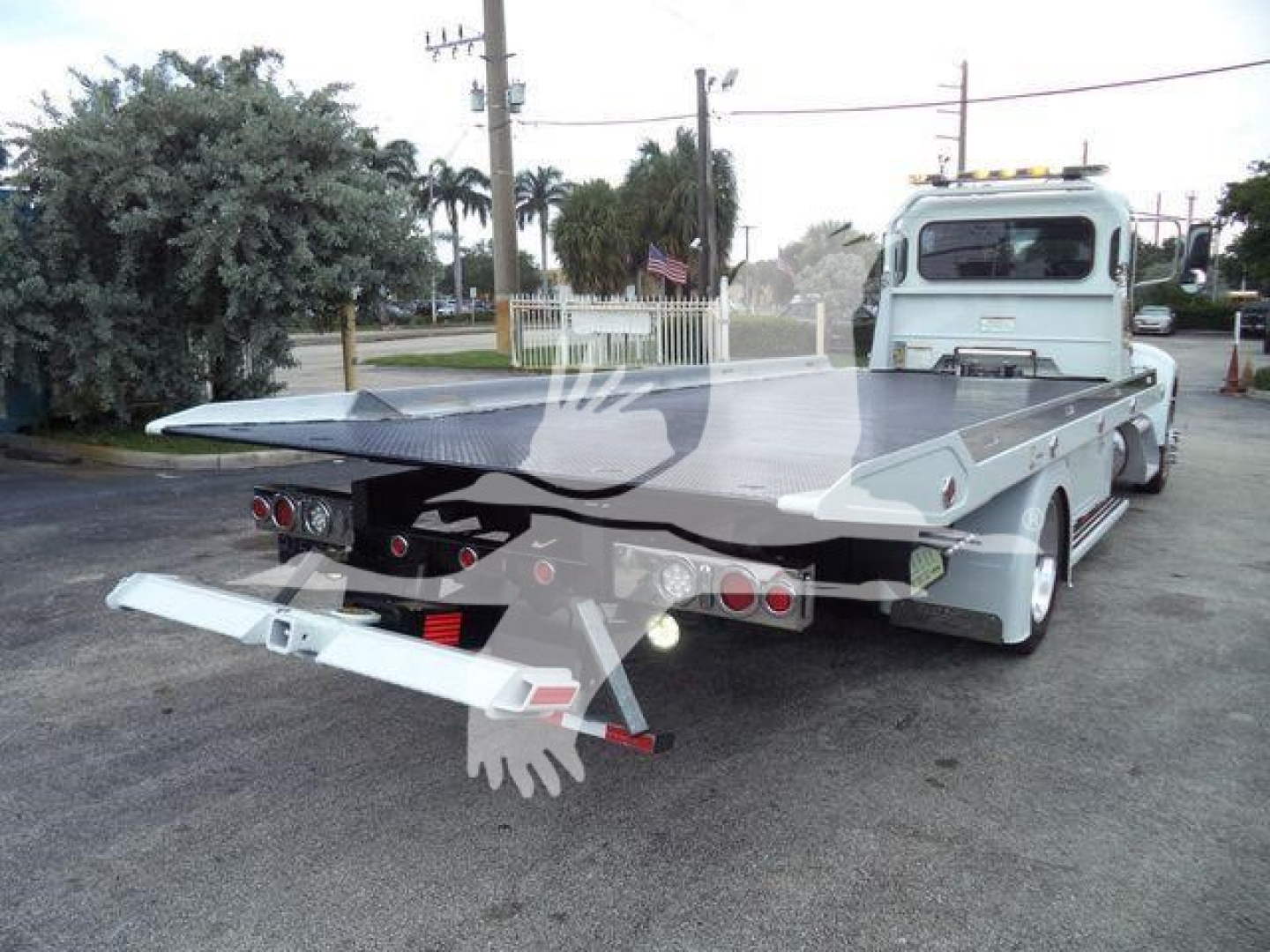Tow truck with a flatbed and rear hydraulic ramps, Peterbilt 337 in background, side and rear views showing platform and lights.