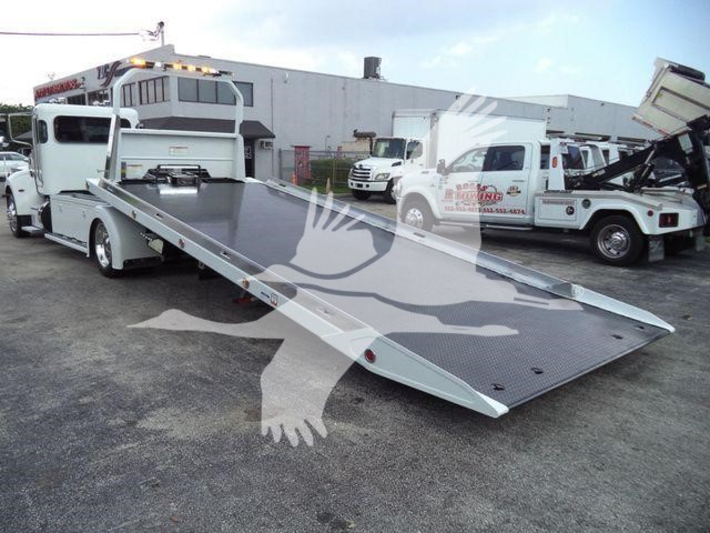 Peterbilt 337 rollback tow truck with a lowered flatbed in view, front cab visible, others in lot.