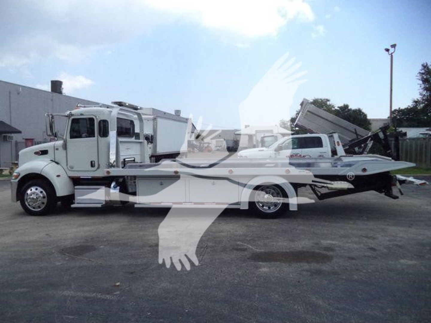 Peterbilt 337 rollback tow truck in yard, white color, side view showing flatbed with ramp and crane, stock number J61994FM.