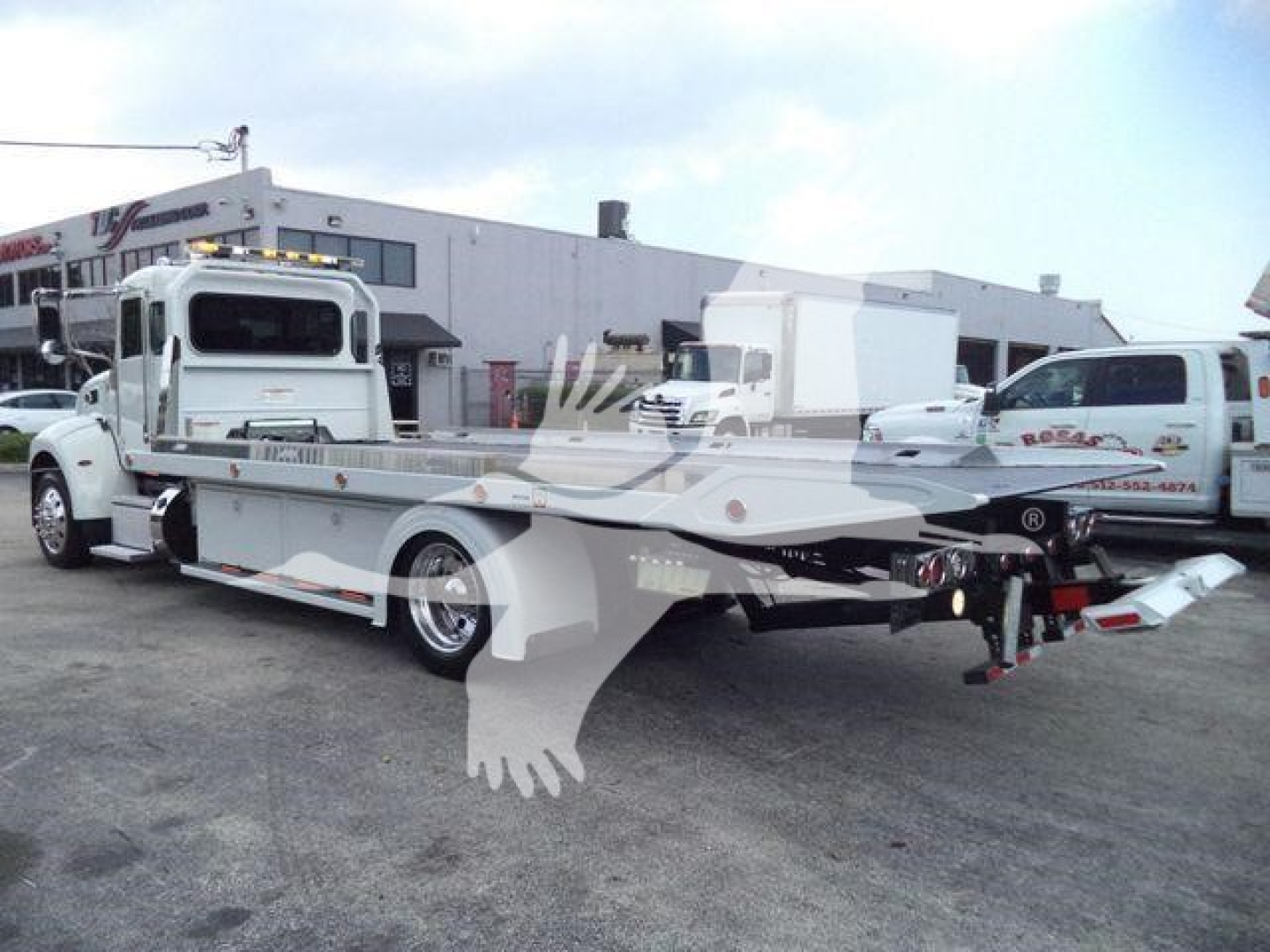Peterbilt 337 rollback tow truck in a parking lot with extended flatbed and hardware visible.