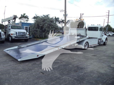 Truck truck bed wrecker-style rollback with a long aluminum ramp extended, Peterbilt 337 cab visible in background, service lot setting.
