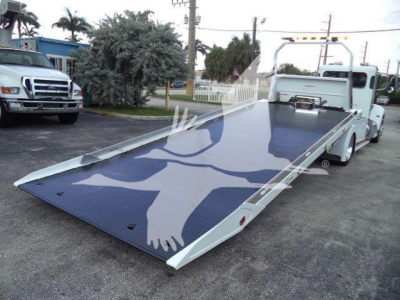 Peterbilt 337 rollback tow truck with lowered flatbed and graphic winged eagle design. Side view shows white cab, long blue tilt/deck platform, rear winch and ramps.