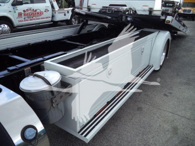 Peterbilt 337 rollback truck side view showing white utility compartments and dual fuel/maintenance tanks, with white body and chrome step rails.