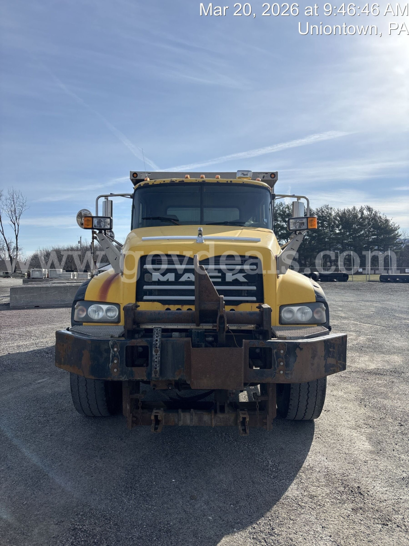 Front view of a yellow Mack GU713 dump truck with black grille and heavy-duty bumper, showing the Mack logo and truck headlights; no visible license plate.
