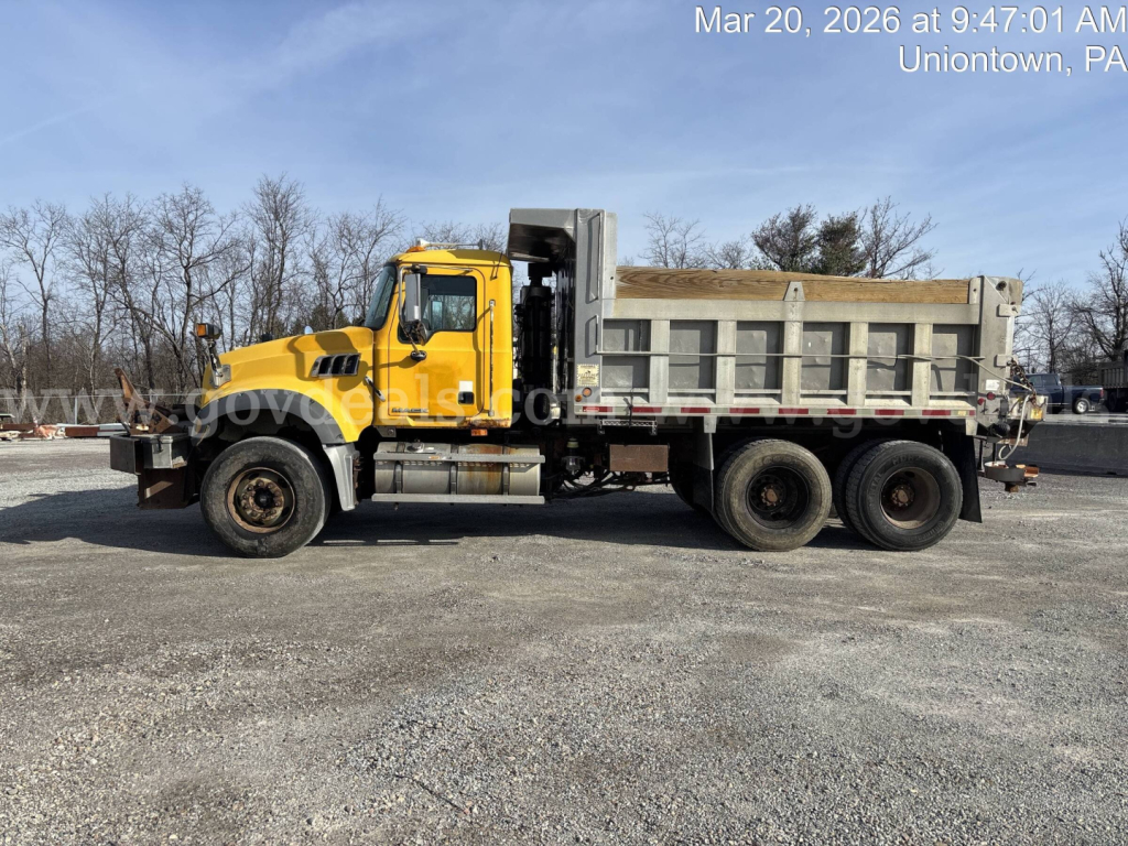 Truck side view showing a yellow Mack GU713 dump truck with open-bed dump body and dual rear wheels.