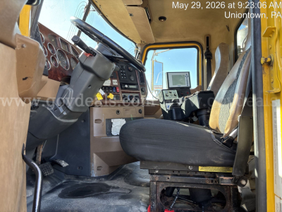 Cab interior of a 2009 Mack GU713 dump truck showing steering wheel, dashboard, driver seat, and passenger seat with mounted display screen.