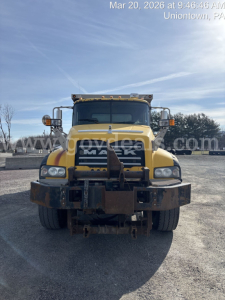 Front view of a yellow Mack GU713 dump truck with black grille and heavy-duty bumper, showing the Mack logo and truck headlights; no visible license plate.