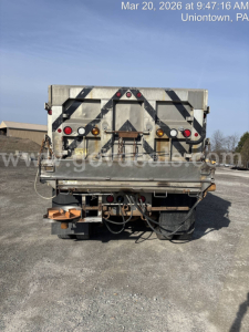 Rear view of a Mack GU713 dump truck showing tailgate with reflective chevrons, multiple lights, and hydraulic lines.