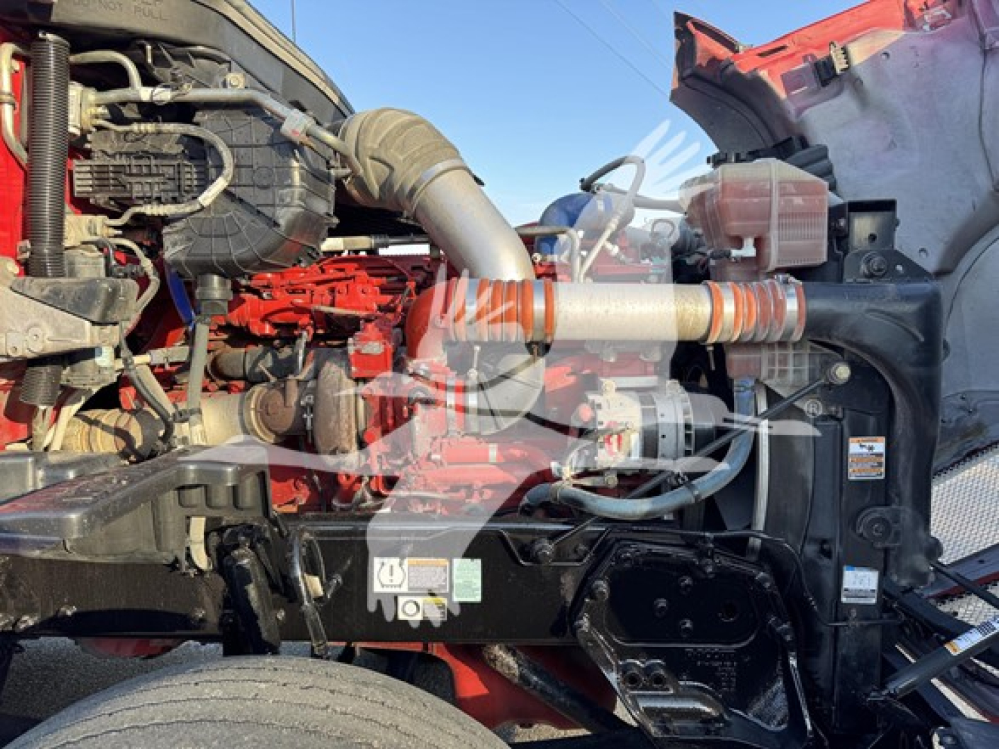 Kenworth T680 engine bay showing red engine block, intake hose, coolant reservoir, and various hoses and components.