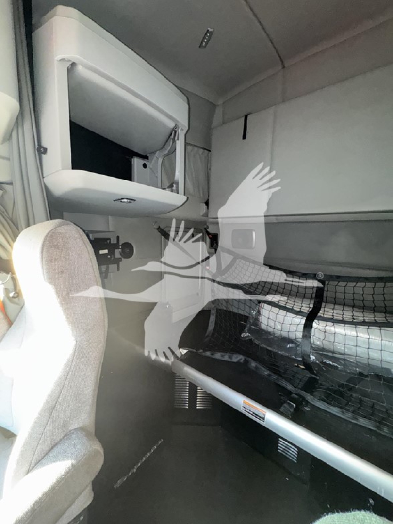 Kenworth T680 sleeper cab interior showing cab area with storage shelf and bunk area, dashboard not visible.