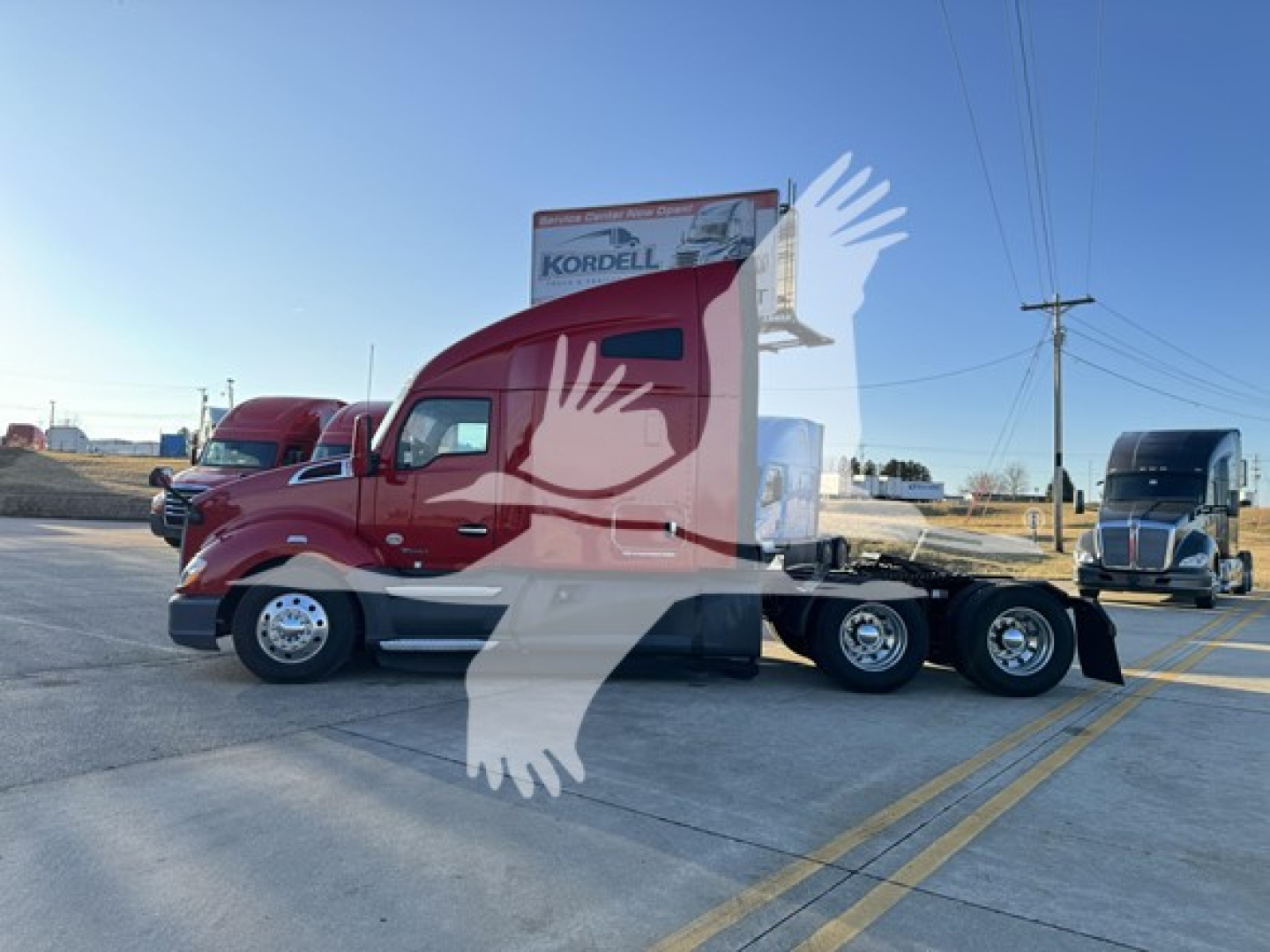 Kenworth T680 tractor in red with a sleeper, side view showing dual rear axles and a long wheelbase; dealership signage in background.
