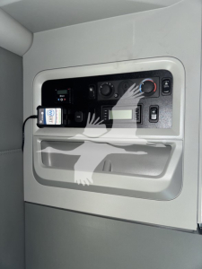 Dashboard panel in a Kenworth T680 sleeper cab showing controls, digital display, and small device plugged into a port.