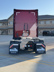 Kenworth T680 rear view showing fifth wheel and mud flaps with logos.