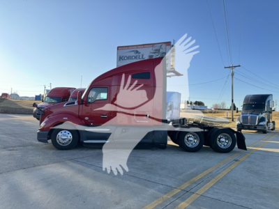 Kenworth T680 tractor in red with a sleeper, side view showing dual rear axles and a long wheelbase; dealership signage in background.