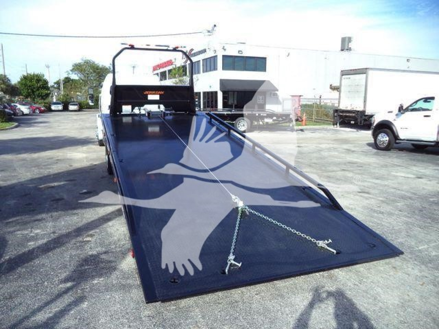 Flatbed tow truck with open ramp on a Freightliner M2 106 Plus chassis, showing a steel loading ramp extended to the ground.