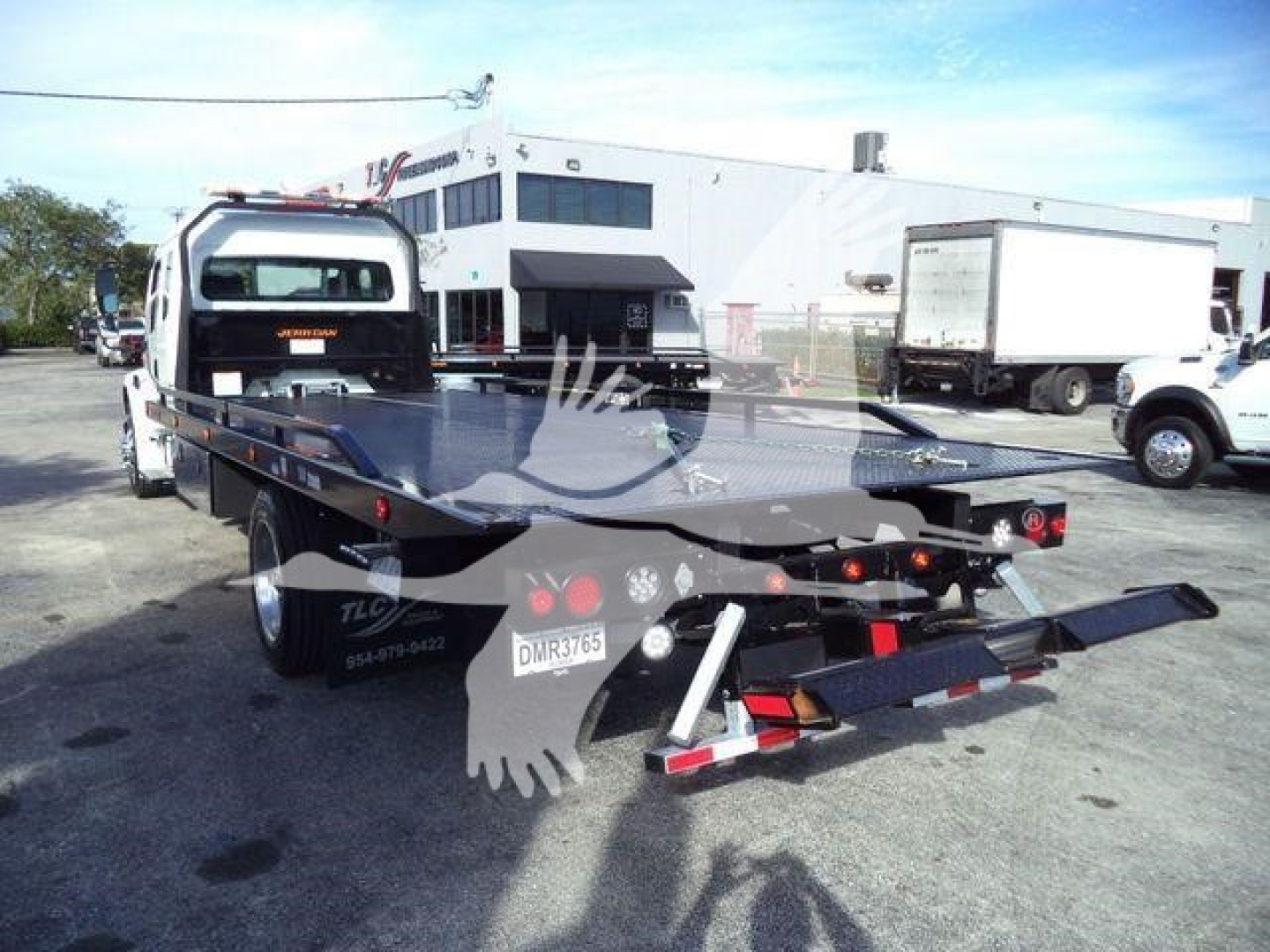 Flatbed rollback truck attached to a Freightliner M2 106 Plus chassis in an outdoor lot showing rear and left side with tow equipment and bumper lights.