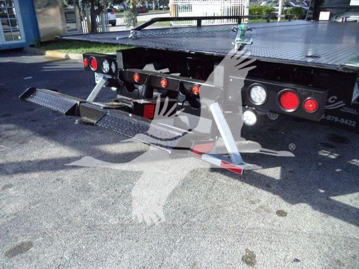 Rear view of a Freightliner M2 106 Plus rollback truck showing twin fold-down asphalt ramps and rear lighting, with platform and bumper details visible.