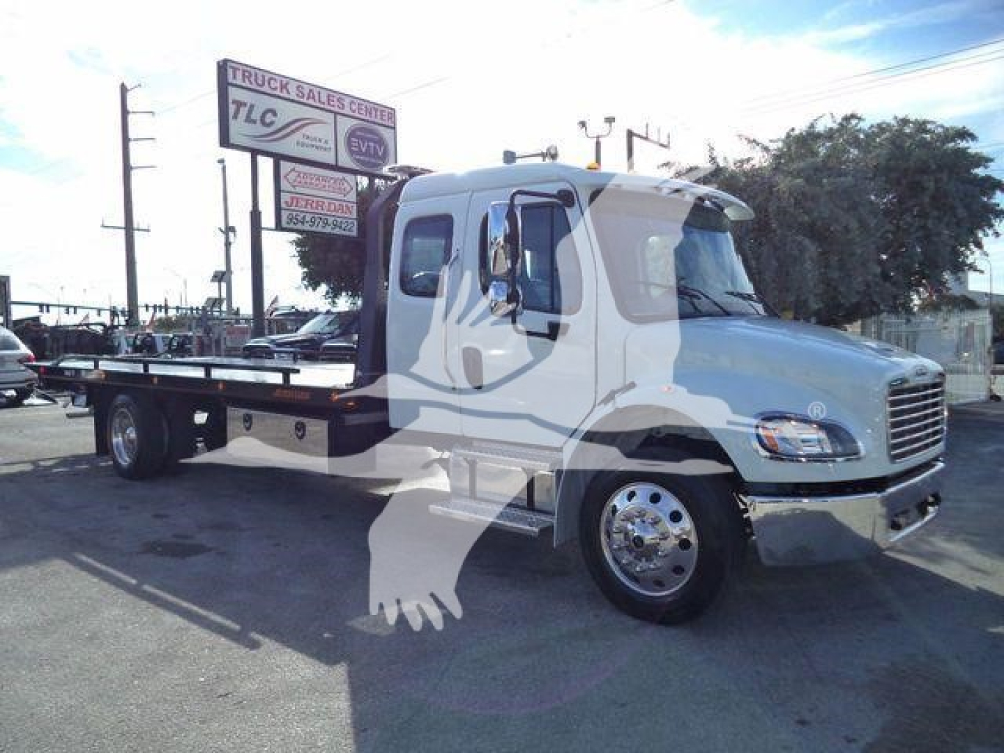 New Freightliner M2 106 Rollback truck front-right view with flatbed, chrome wheels, and signage in background.