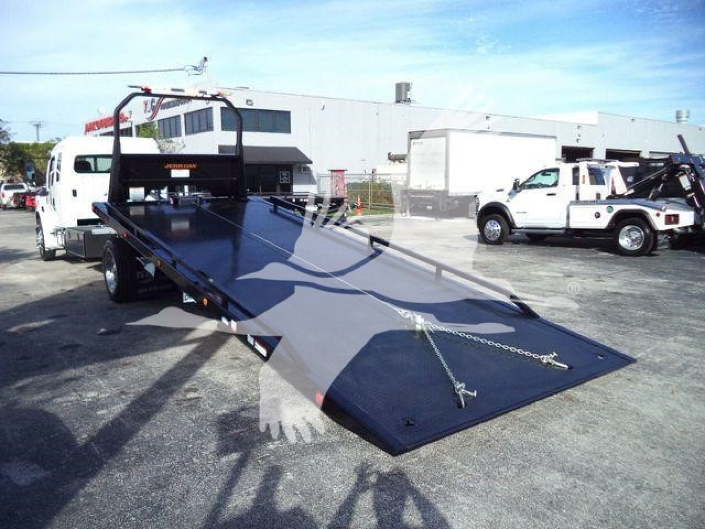 Trailer/rollback ramp with loading platform and chain tie-downs, Freightliner M2 106 Plus dealership lot in background.
