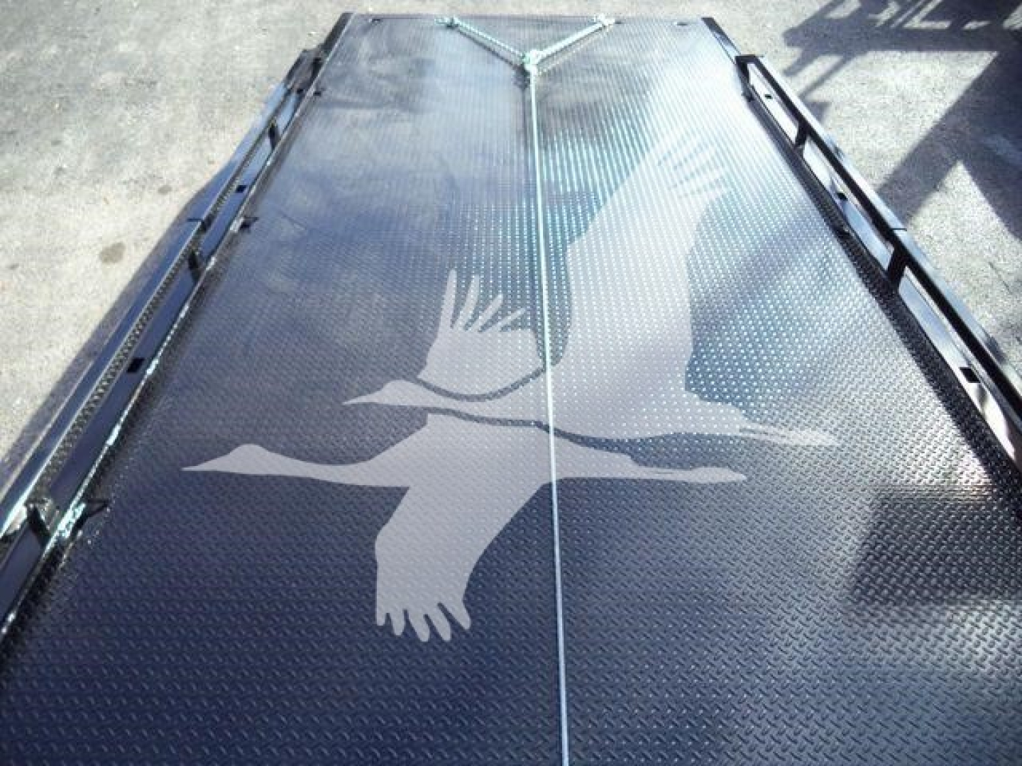 All-metal truck bed or loading platform with diamond plate texture and bird graphic silhouette in light gray against dark surface.