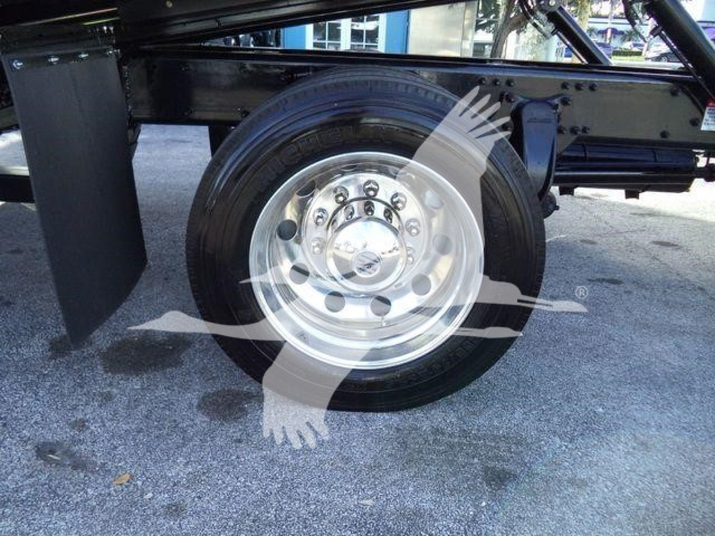 Wheel and tire assembly of a Freightliner M2 106 Plus truck showing a polished steel wheel and circular lug pattern under a rollback chassis.