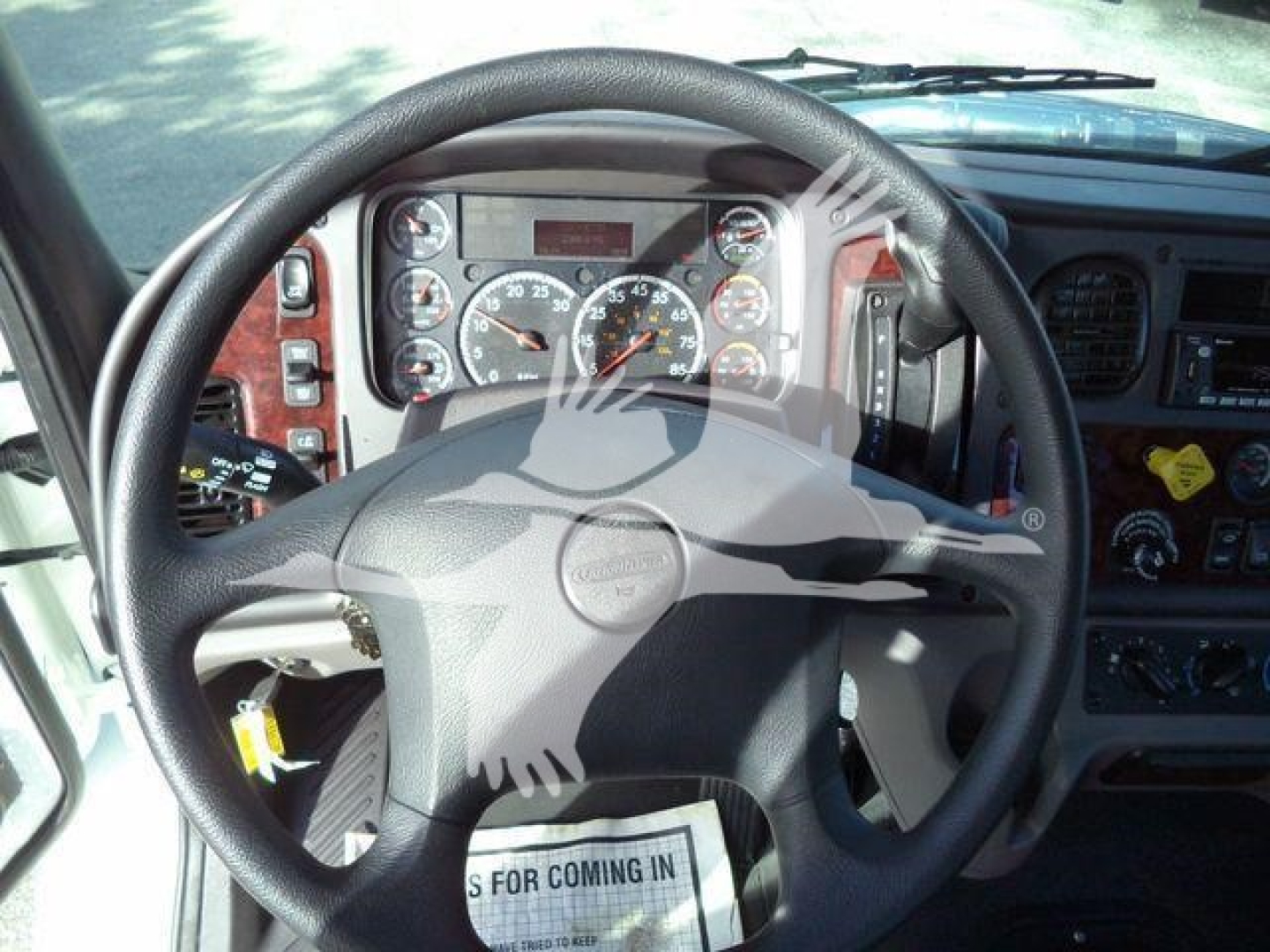 Truck cabin steering wheel and instrument cluster showing analog gauges; center display; dashboard panels with various switches and vents.