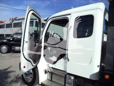 Truck cab with driver door open, showing interior and steps; white Freightliner M2 106 Plus roll-back truck in a dealership lot.