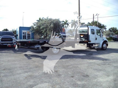 Flatbed tow truck in a lot with Freightliner M2 106 Plus cab visible from side, showing wheelbase and flatbed platform.