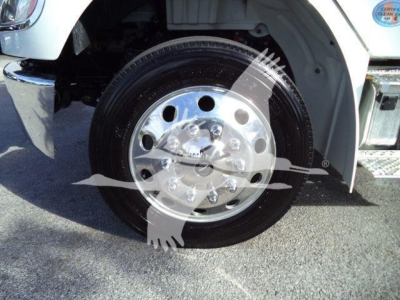 Front wheel of a Freightliner M2 106 Plus truck showing chrome alloy wheel and tire, with part of the white fender and side chrome bumper.