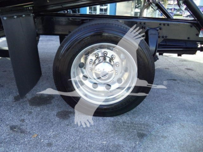 Wheel and tire assembly of a Freightliner M2 106 Plus truck showing a polished steel wheel and circular lug pattern under a rollback chassis.