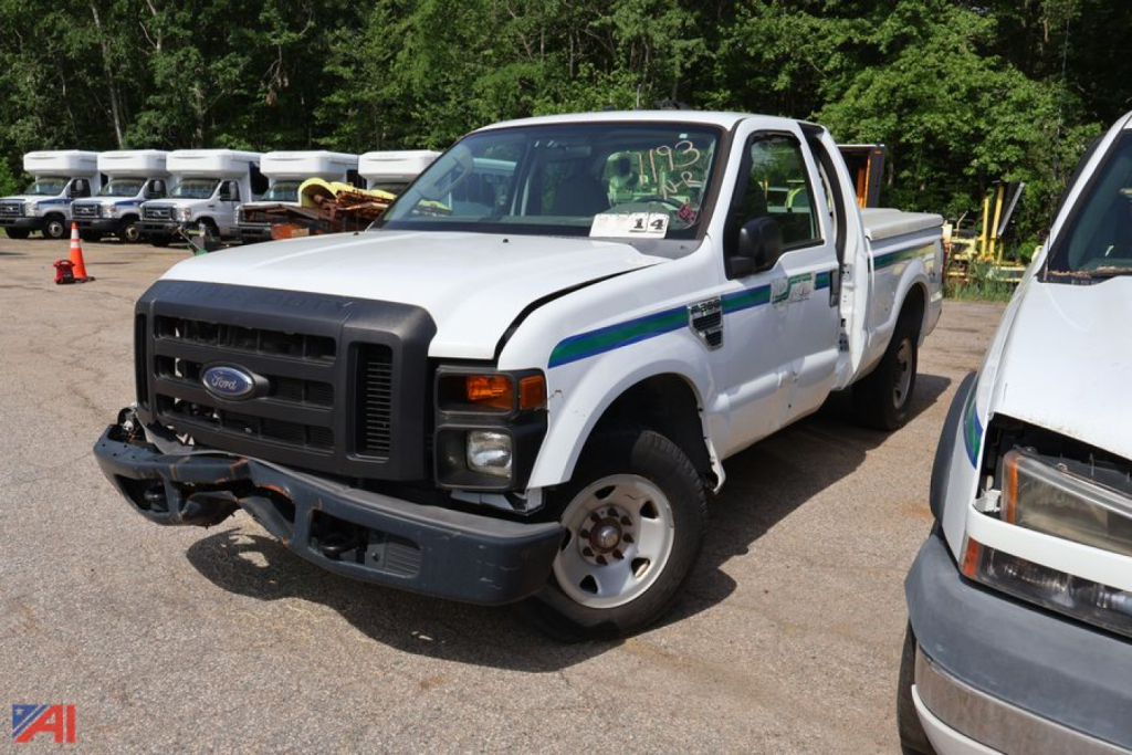 Ford F-250 Super Duty pickup truck in a yard, white with blue/green stripe, front bumper damaged, right side cab door open, other vehicle nearby.