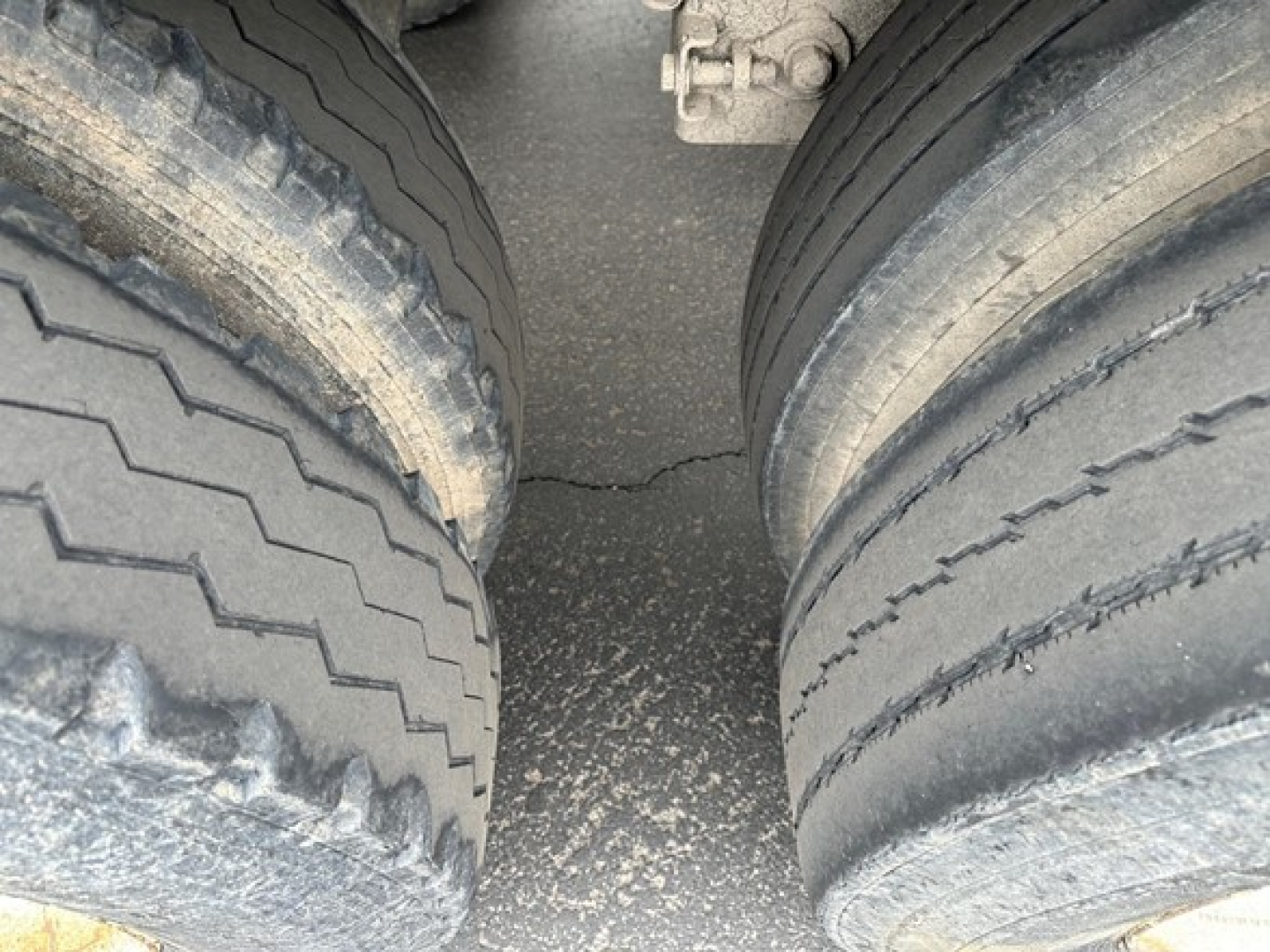 Dual-axle trailer tires in view with wear patterns, shared frame between wheels, concrete surface beneath.