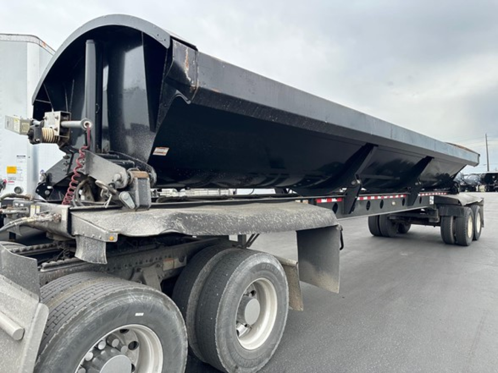 Trailer side dump bed with hydraulic overhang and wheels; no legible labels visible on the image