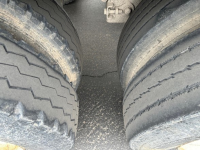 Dual-axle trailer tires in view with wear patterns, shared frame between wheels, concrete surface beneath.