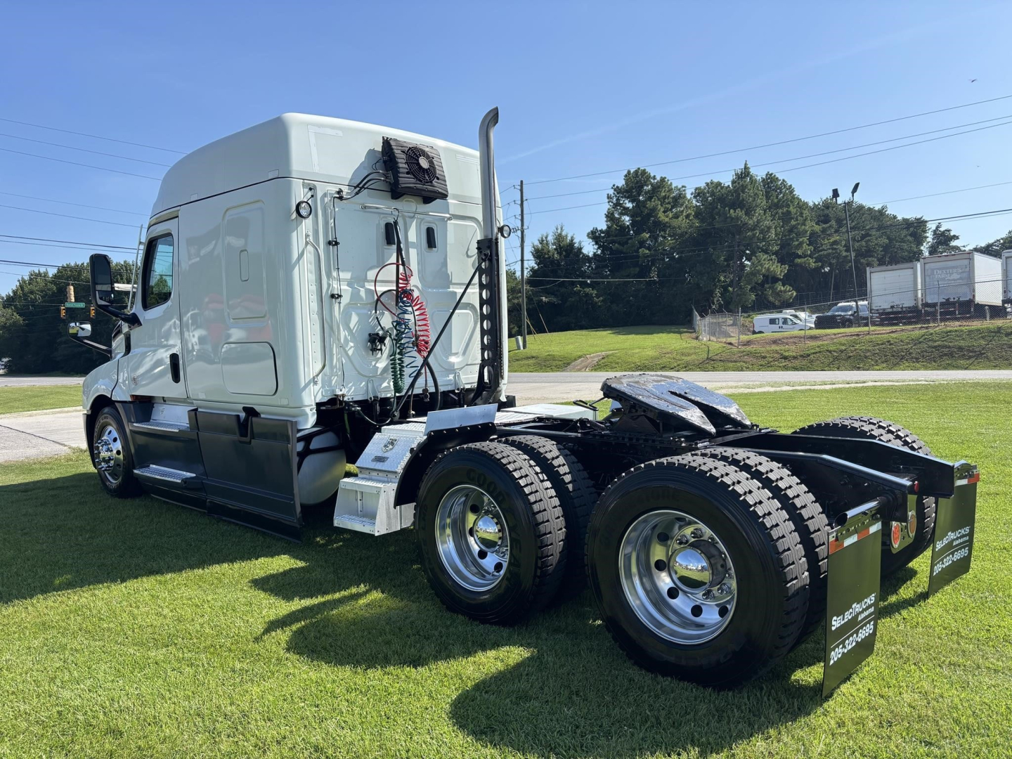 Freightliner Cascadia 126 sleeper tractor from left-rear angle showing dual rear axles, white tractor cab, external air tanks, exhaust stack, and fifth-wheel with mudflaps.