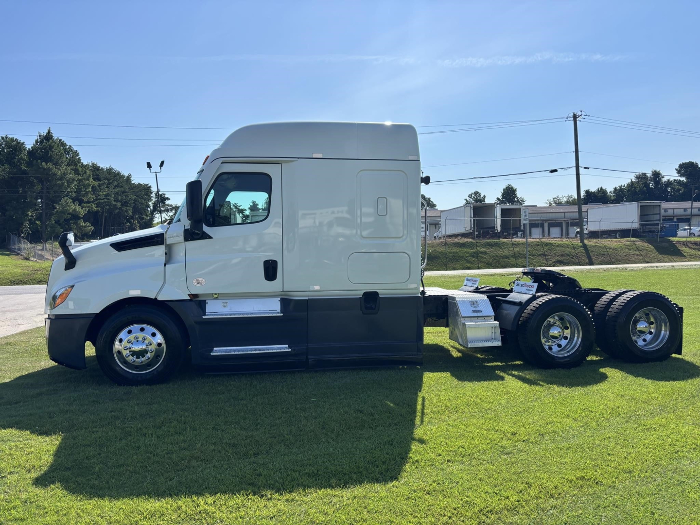 Truck side view of a 2021 Freightliner Cascadia 126 sleeper cab with empty trailer chassis and MV green grass.
