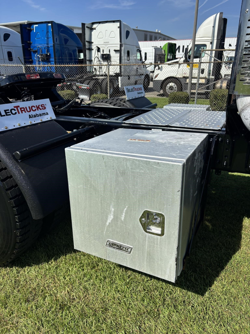 Aluminum toolbox mounted on side of Freightliner Cascadia truck chassis with fuel/air tanks and parked trailers in background.