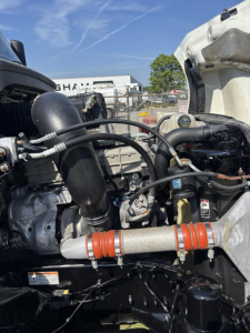 Engine bay view of a 2021 Freightliner Cascadia 126 with components including turbocharger, intercooler hoses, coolant reservoir, piping, and a copper-colored exhaust or coolant line, various hoses and clamps visible