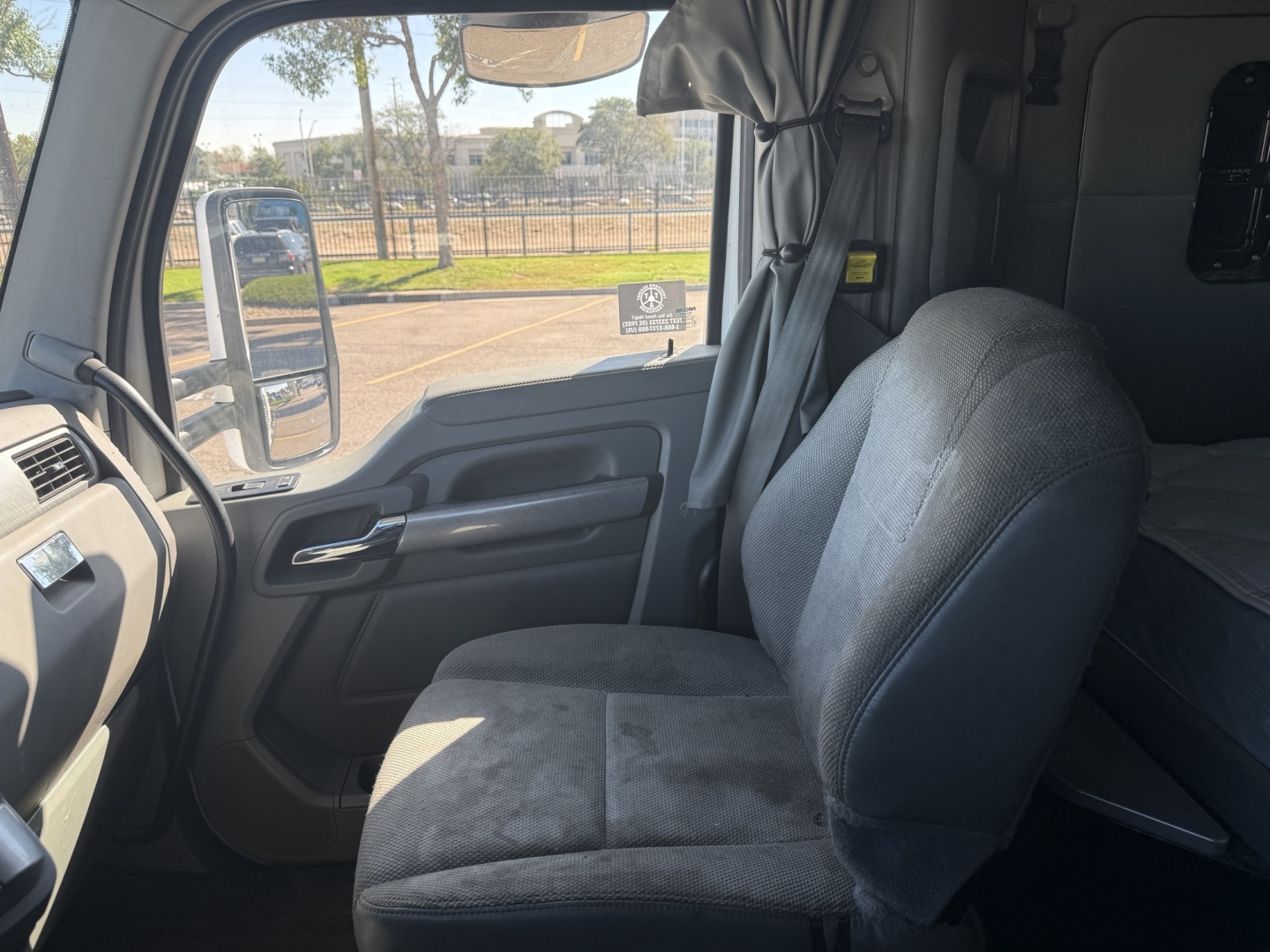 Kenworth T880 cab interior left-side dash and driver seat in view, with window and mirror reflections.