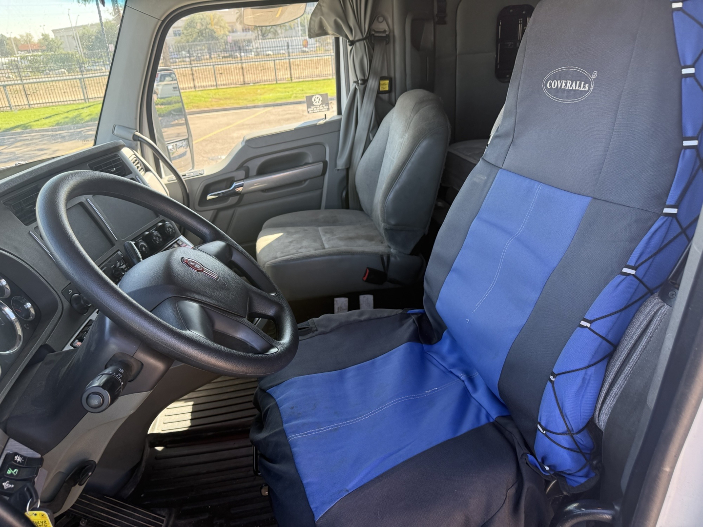 Kenworth T880 cab interior showing steering wheel, driver seat with blue/gray seat cover, dashboard, and passenger seat.
