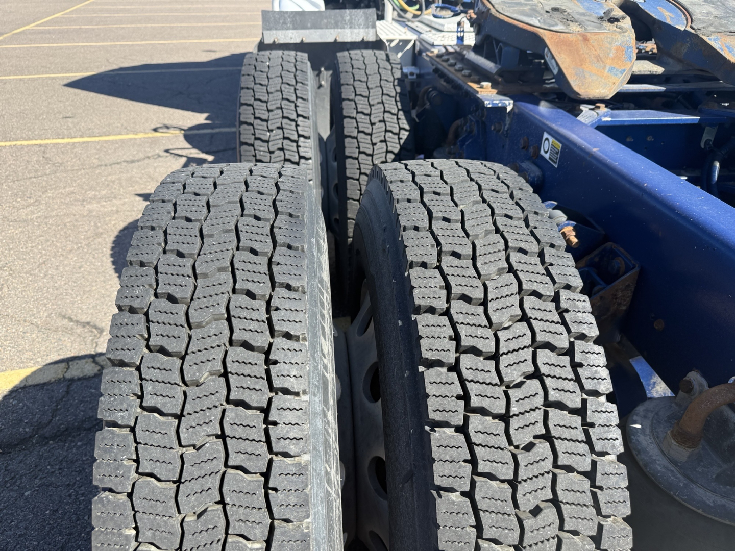Kenworth T880 truck chassis showing dual rear axles with quad tires and tread pattern, part of a cab-over style yet visible on a parking lot.