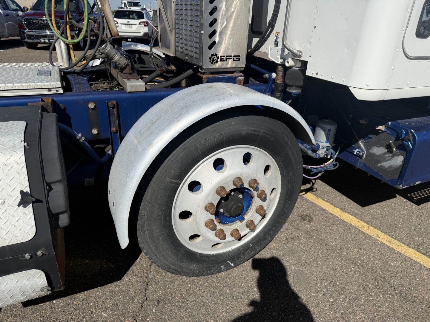 Kenworth T880 front wheel and fender close-up showing wheel with lug nuts and fender; part of truck cab and chassis visible.