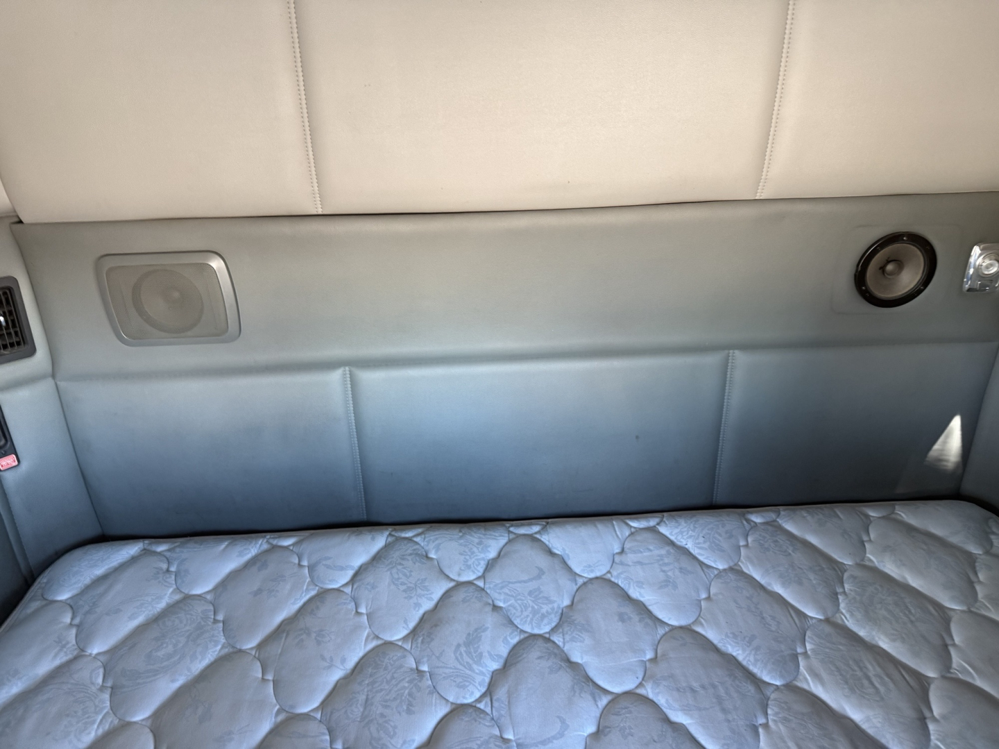 2016 Kenworth T880 sleeper truck interior with light gray upholstery and quilted mattress; side panel shows a speaker and small round vent; upper area has seatback and lighting.