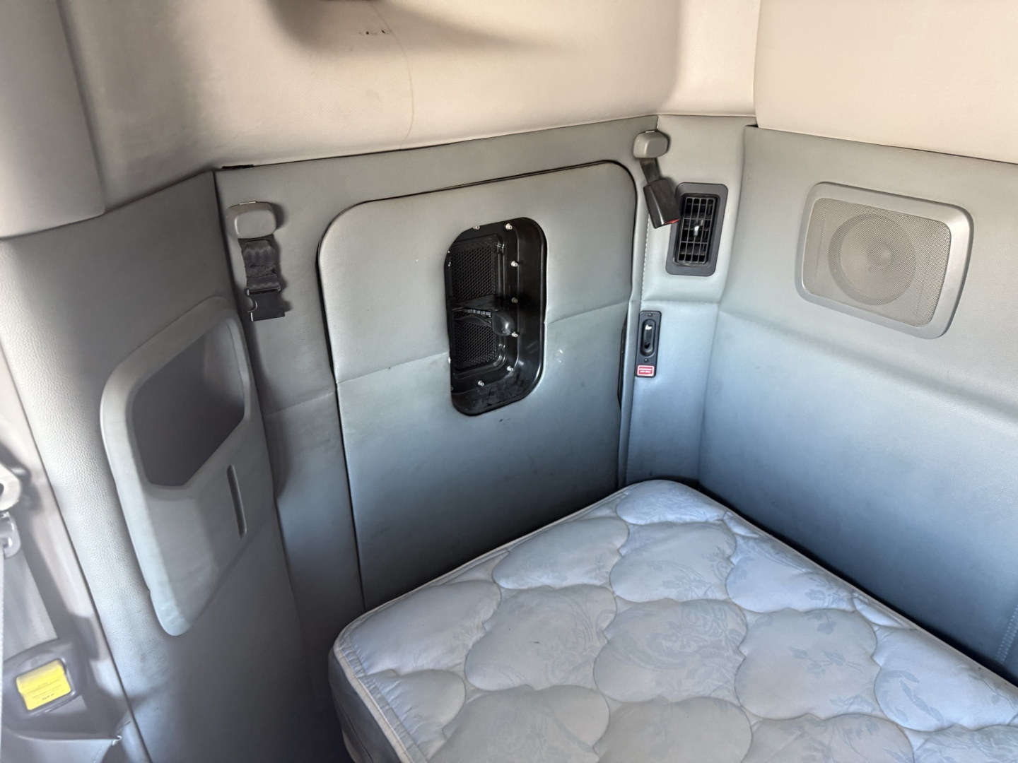 Kenworth T880 sleeper cab interior showing side wall with storage pocket and window vent, quilted seat cushion, and control panel area