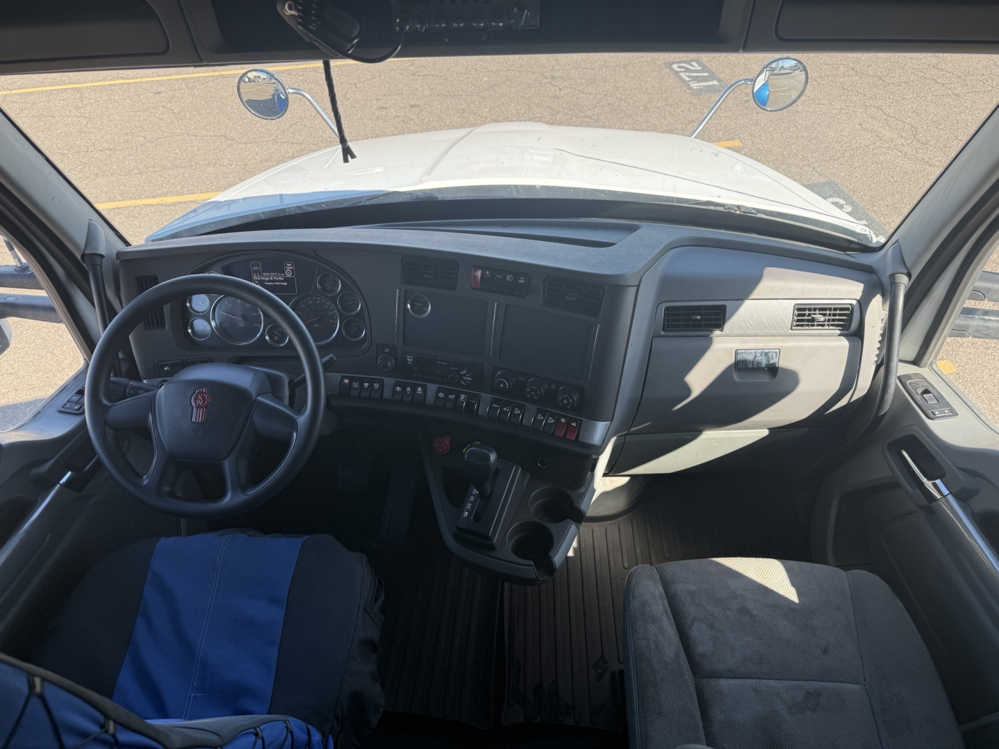 Kenworth T880 cab interior showing steering wheel with logo, dashboard controls, and driver seat with blue cover.